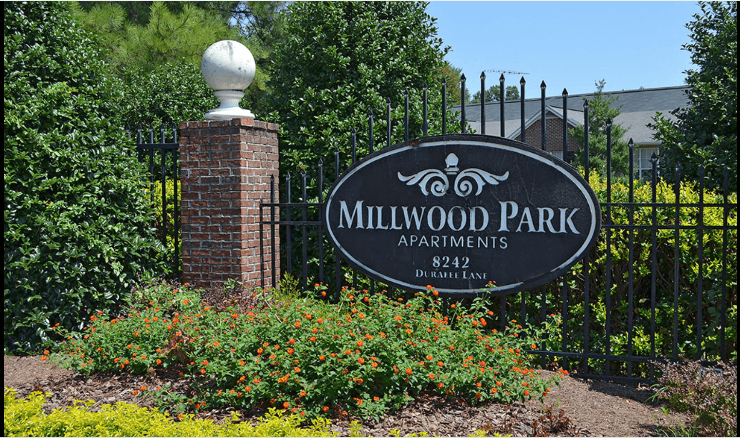 A sign for Millwood Park apartments stands in front of a fence.